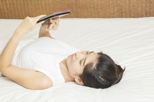 happy young asian woman lay down and working on tablet in bedroom