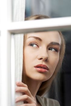 Beautiful woman is looking through window. Indoor background.