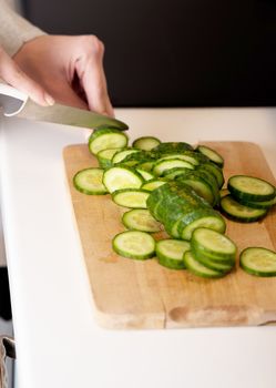 Woman in cutting fresh green cucumber on kitchen board.