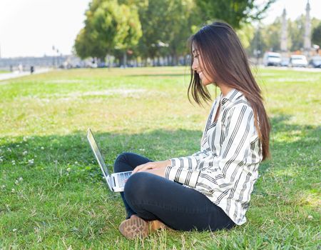 Beautiful asian girl using a laptop sitting on the grass