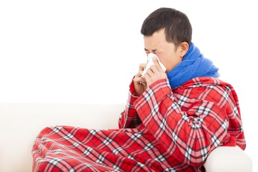 ill man blowing nose with tissue on sofa