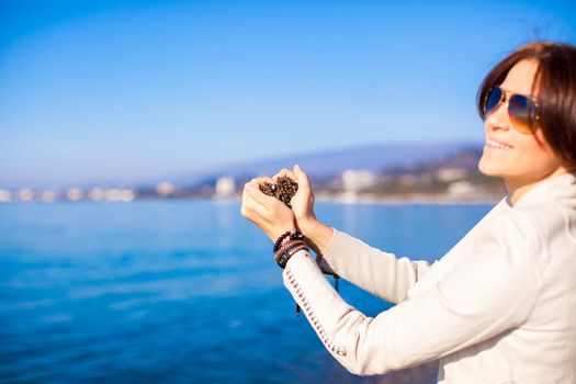 Woman hands holding small stones form heart shape background the sea