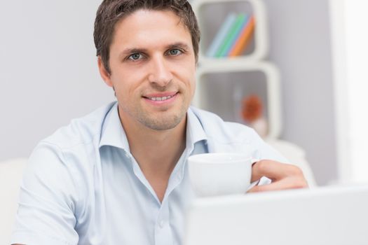 Close-up of man with teacup using laptop at home