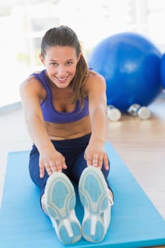 Full length portrait of a sporty young woman stretching hands to legs in fitness studio