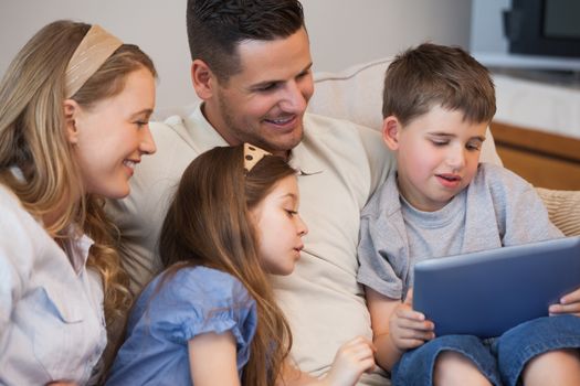 Happy family of four using digital tablet in living room