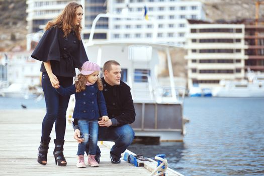 Portrait of happy young family walking with their child on berth near sea in the city, still life photo