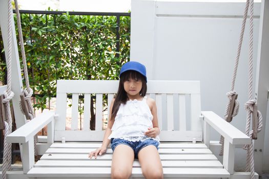 girl sitting on a swing Blue hat sitting on white wooden swings.