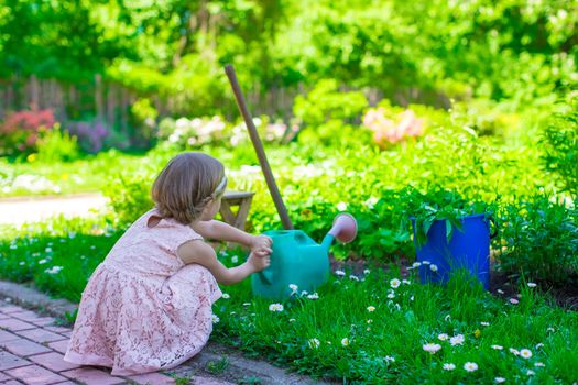 Adorable cute girl with a watering can at big green garden