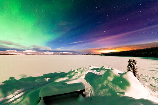 Spectacular display of Northern Lights or Aurora borealis or polar lights and light pollution from itself not visible city of Whitehorse over frozen Lake Laberge, Yukon Territory, Canada, moon-lit winter landscape