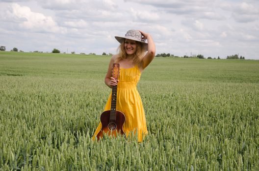 women yellow dress and guitar pose in rye field