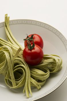 Dried Italian tagliatelli pasta and fresh tomatoes ready in a white ceramic bowl to be used as ingredients in preparing a traditional pasta recipe, close up high angle view