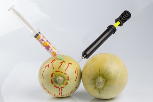 Cosmetic treatment  for Female breasts metaphor: melons with perforation lines while  air pumped  by bicycle pump and injected by a syringe with pillsmeaning cosmetic and health treatment