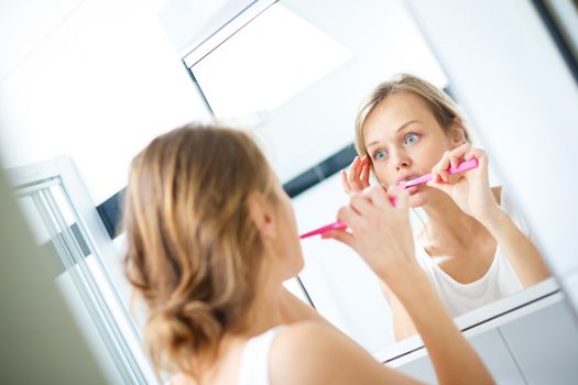 Pretty female brushing her teeth in front of mirror in the morning, making silly faces, checking her skin