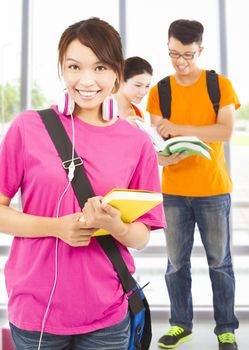 pretty young student holding books and earphone with classmates