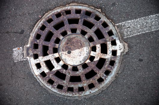 Manhole with metal cover in asphalt with white road marking line
