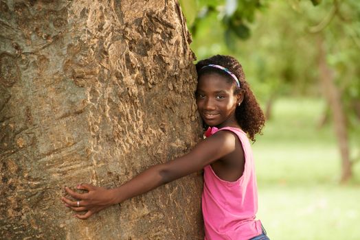 Portrait of black ecologist girl hugging tree and smiling