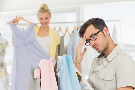 Bored man with shopping bags while woman at clothes rack