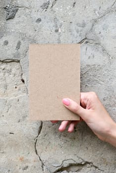 Greeting card in woman hand on wall background