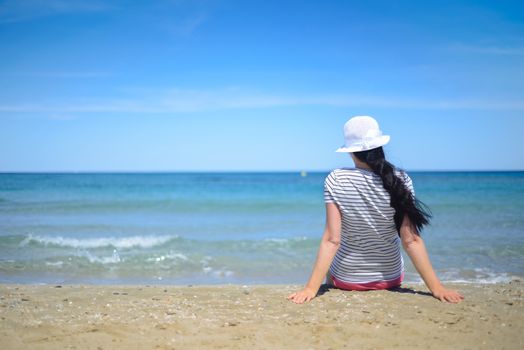 Young brunette  woman sitting on sand and looking to a sea