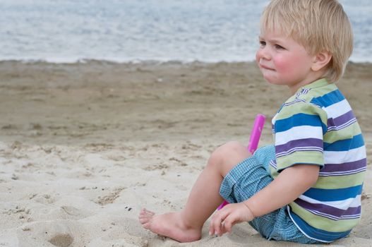 Little toddler boy sitting on sand beach