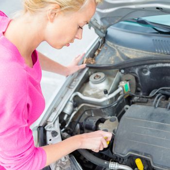Self-sufficient confident modern young woman checking level of the engine oil in the car.