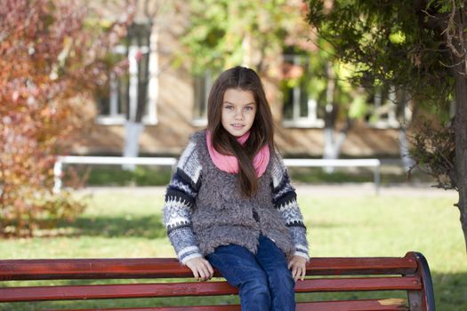 Beautiful little girl sitting on a bench 