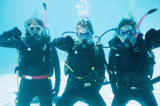 Friends on scuba training submerged in swimming pool showing thumbs down