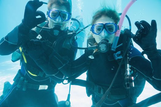 Friends on scuba training submerged in swimming pool looking to camera