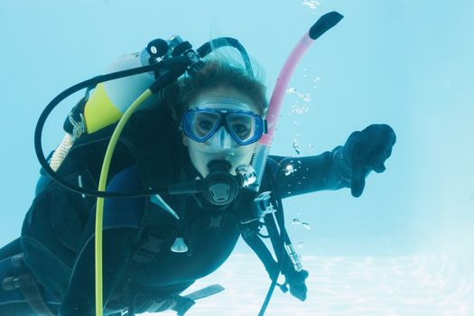Woman on scuba training submerged in swimming pool showing thumbs down