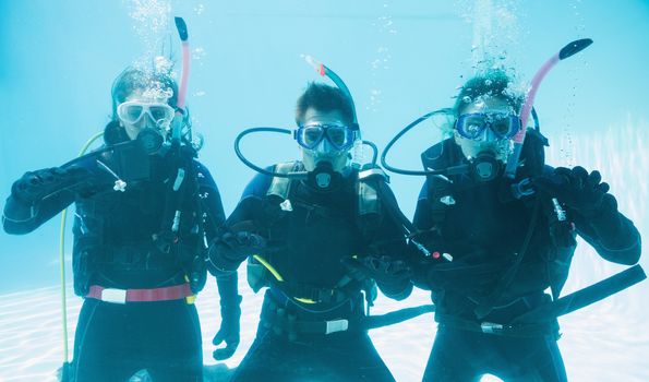 Friends on scuba training submerged in swimming pool making ok sign