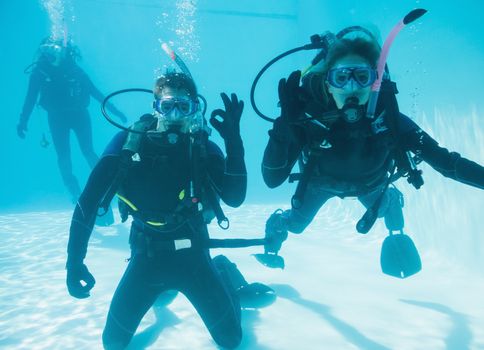 Friends on scuba training submerged in swimming pool two looking to camera
