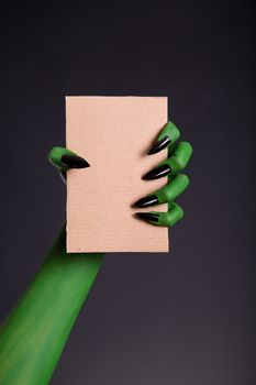 Green monster hand with black nails holding blank piece of cardb