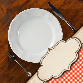 Restaurant menu with empty white plate with silver cutlery, on wooden background with red and white tablecloth and empty label