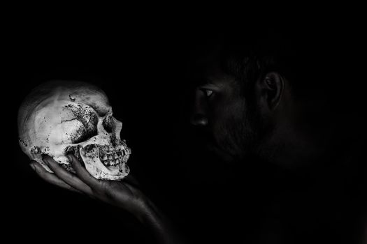 Man in shadow stare human skull that hold in hand 
