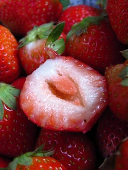 A cut delicious strawberry on a stack of fresh ripe strawberries.