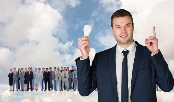 Composite image of businessman holding light bulb and pointing