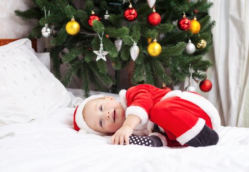 Baby boy in Santa costume lying on bed