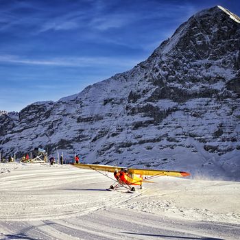 Yellow airplane landing to  alpine resort in swiss alps in winte