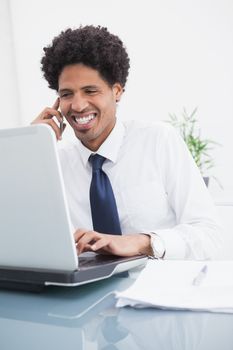 Smiling businessman on the phone and using laptop