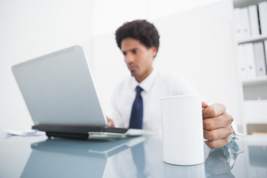 Businessman using laptop and holding mug at desk