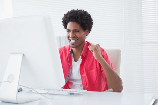 Smiling casual businessman cheering at his desk