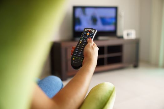 Woman on sofa watching tv changing channel with remote