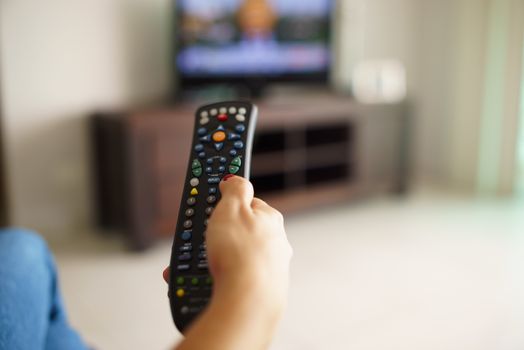 Woman sitting watching tv changing channel with remote