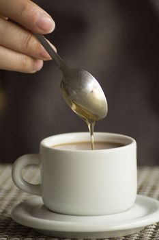Hand and spoon corn syrup in cup of coffee expresso