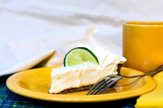 Slice of key lime pie with coffee closeup on plate with fork and napkin.