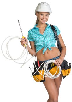 Pretty electrician in helmet, shorts, shirt, tool belt with tools holding screwdriver and an electric cable