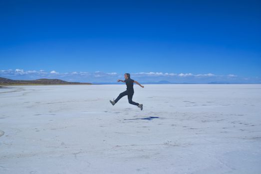 Young man jumps on vast salt plane Salar de Uyuni in Bolivia