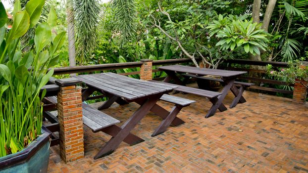 Wooden chairs and table set at balcony in a green plant garden.