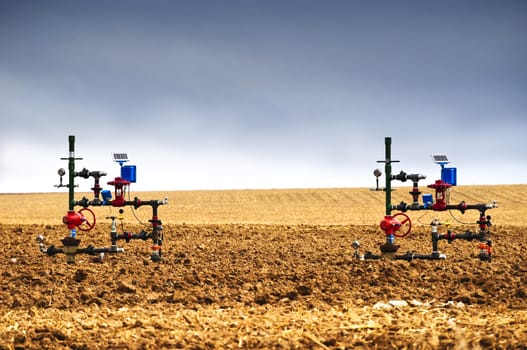 Natural gas wellheads close together in a plowed cornfield.