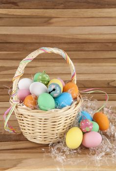 colorful easter eggs and bells in wicker basket on wooden background